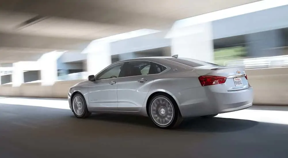 A silver 2020 Chevy Impala is driving on a blurred, covered highway.