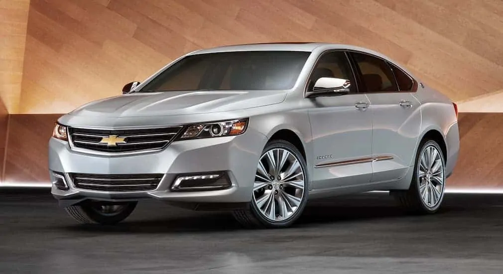 A silver 2020 Chevy Impala is in a showroom with a wooden wall.