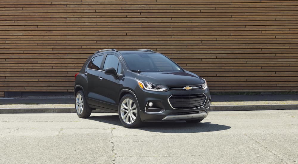 A dark grey 2020 Chevy Trax is parked in front of a wooden wall after winning the 2020 Chevy Trax vs 2020 Buick Encore comparison.