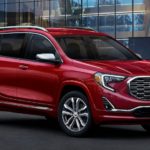 A red 2020 GMC Terrain is parked in front of a glass building after winning the 2020 GMC Terrain vs 2020 Mazda CX-5 comparison.