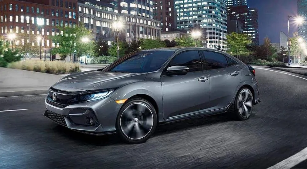 A gray 2020 Honda Civic Hatchback Sport Touring is driving in a city at night.