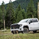 A white 2020 GMC Sierra 2500HD AT4 is parked in front of trees and a mountain.