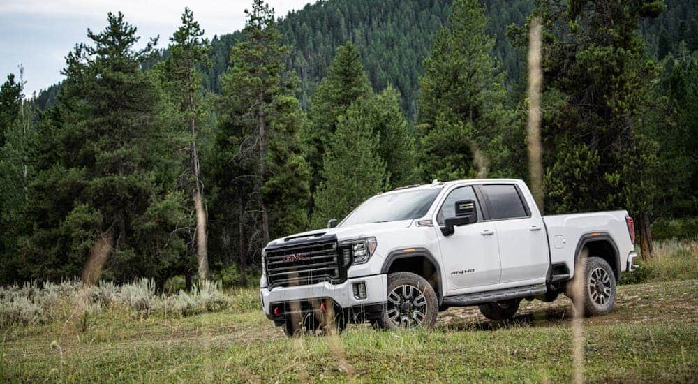 A white 2020 GMC Sierra 2500HD AT4 is parked in front of trees and a mountain.