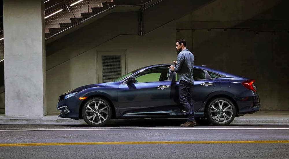 A man is walking to his blue 2020 Honda Civic Sedan Sport that is parked under an overpass.