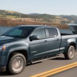 A grey 2020 Chevy Colorado LT is towing a boat past a lake after winning the 2020 Chevy Colorado vs 2020 Ford Ranger comparison.
