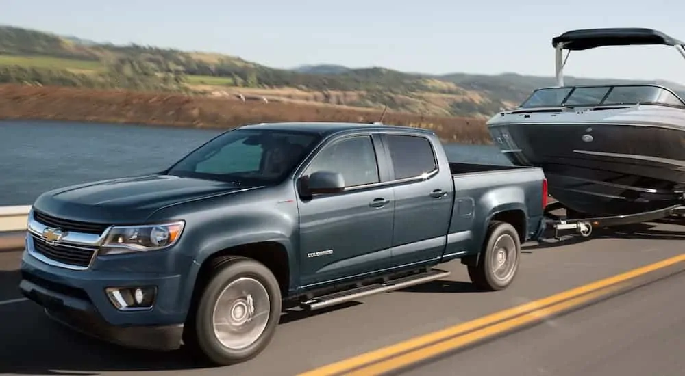 A grey 2020 Chevy Colorado LT is towing a boat past a lake after winning the 2020 Chevy Colorado vs 2020 Ford Ranger comparison.