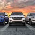 A blue, a white and a silver 2020 Jeep Compass are shown from the front against a vibrant orange sunset.