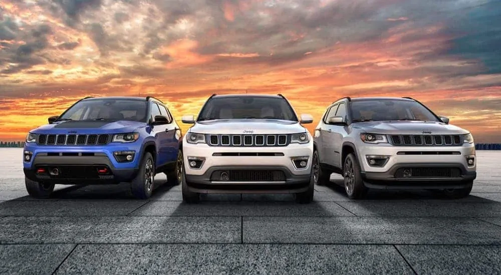 A blue, a white and a silver 2020 Jeep Compass are shown from the front against a vibrant orange sunset.