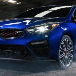 A blue 2020 Kia Forte is parked in a warehouse with a dirt floor.