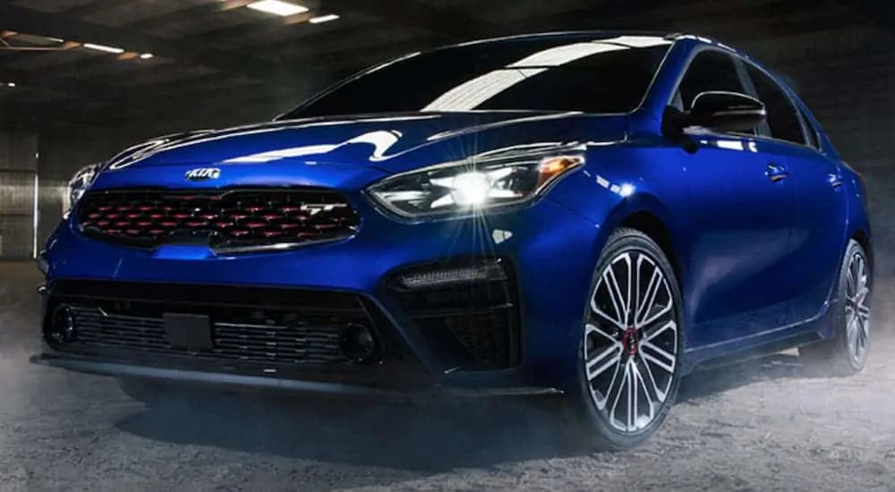 A blue 2020 Kia Forte is parked in a warehouse with a dirt floor.