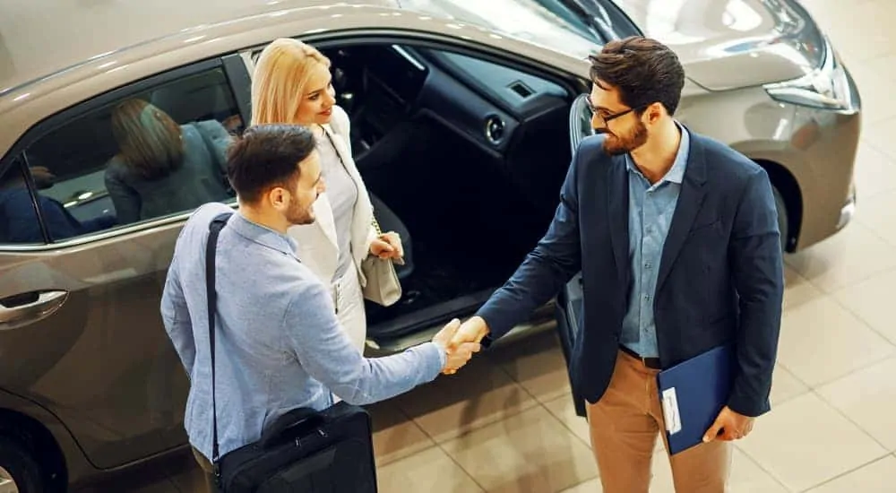 A couple is shaking the hand of a salesman after doing an end of lease turn-in.