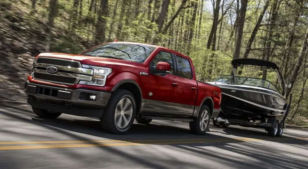 A red 2020 Ford F-150, which is popular among Ford trucks, is towing a boat on a tree-lined road.