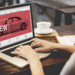 A woman is looking at a new car on a laptop while online car shopping.