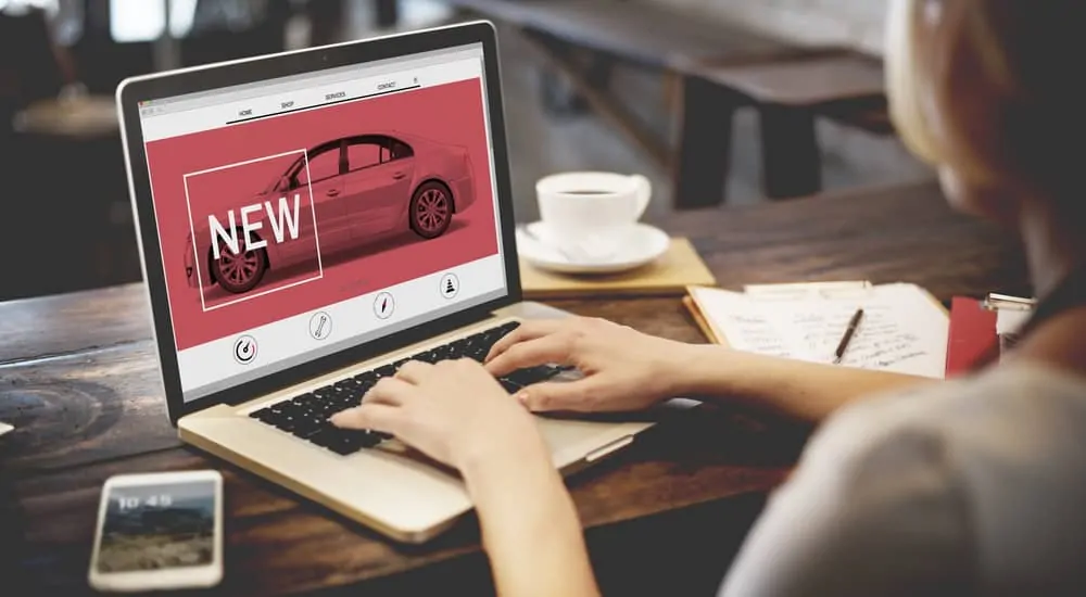 A woman is looking at a new car on a laptop while online car shopping.