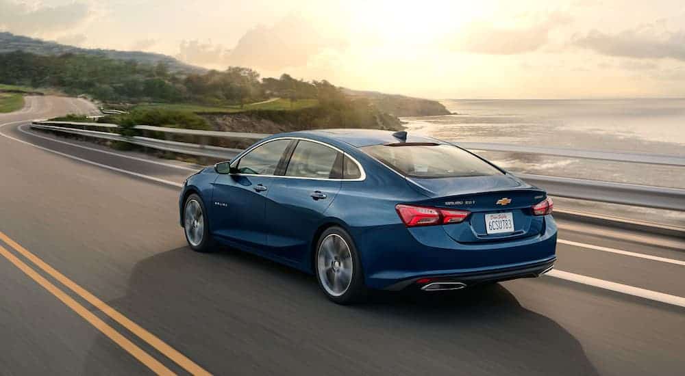 A blue 2020 Chevy Malibu is driving along an ocean bay.