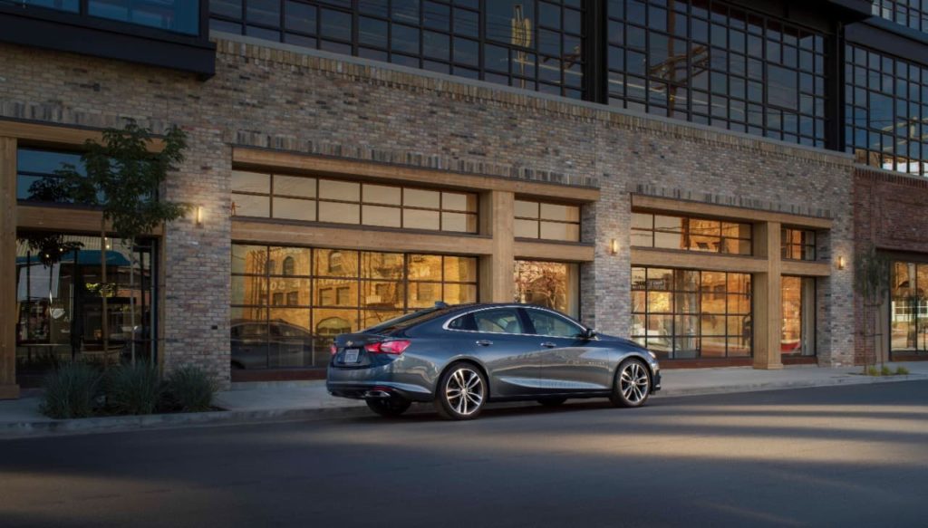 A gray 2020 Chevy Malibu is parked in front of a white brick building.