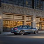 A gray 2020 Chevy Malibu is parked in front of a white brick building.