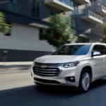 A white 2020 Chevy Traverse High Country is driving on a city street after winning the 2020 Chevy Traverse vs 2020 Ford Explorer comparison.