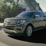 A gray 2020 Ford Expedition Platinum is driving on a suburban street.