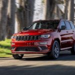 A red 2020 Jeep Grand Cherokee is driving on a tree-lined road.