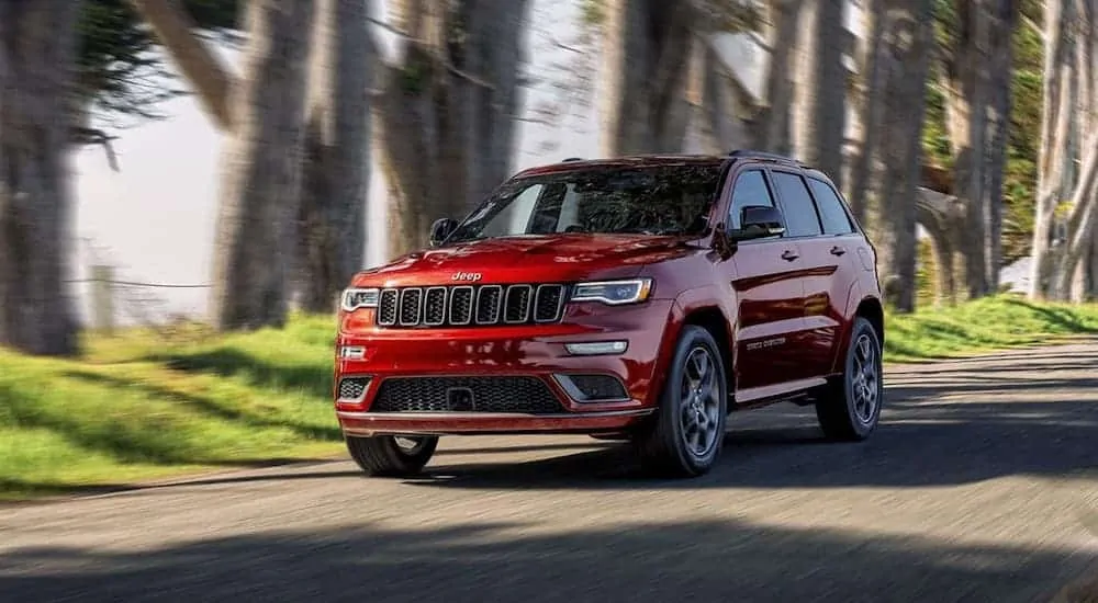 A red 2020 Jeep Grand Cherokee is driving on a tree-lined road.