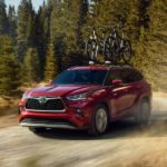 A burgundy 2020 Toyota Highlander Hybrid is driving on a dirt road with bikes on the roof.