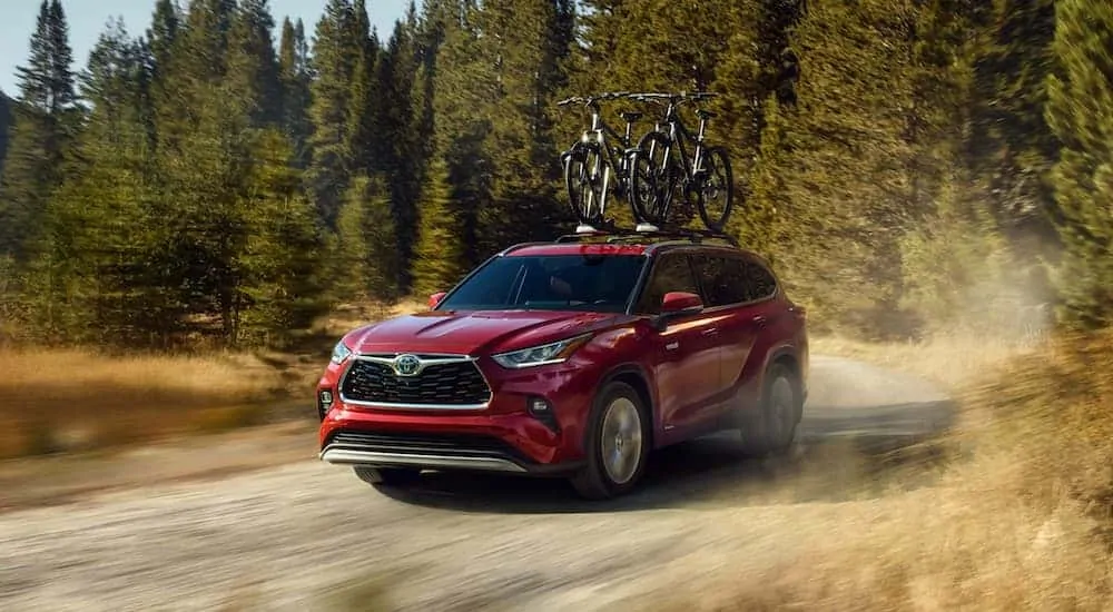 A burgundy 2020 Toyota Highlander Hybrid is driving on a dirt road with bikes on the roof.