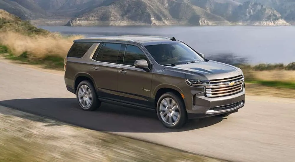 A grey 2021 Chevy Tahoe is driving past a body of water after winning the 2021 Chevy Tahoe vs 2020 Chevy Tahoe comparison.