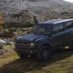 A black 2021 Ford Bronco is off-roading on a grassy trail.