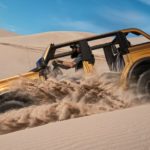 An orange 2021 Ford Bronco is shown from the side off-roading on a sand dune.