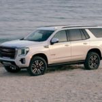 A white 2021 GMC Yukon AT4 is parked at a beach after showing the new trim available on the 2021 GMC Yukon vs 2020 GMC Yukon.