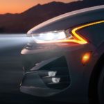 A closeup shows the front quarter of a white 2021 Kia K5 from the side at night.