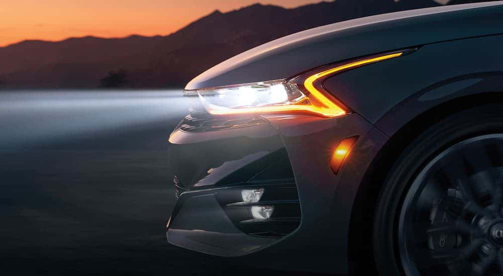 A closeup shows the front quarter of a white 2021 Kia K5 from the side at night.