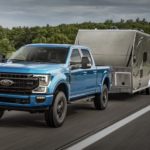 A blue 2020 Ford Super Duty, one of the popular a popular Ford trucks for sale, is towing a camper on a highway.