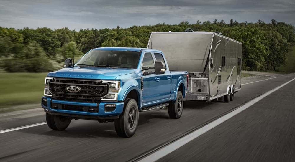 A blue 2020 Ford Super Duty, one of the popular a popular Ford trucks for sale, is towing a camper on a highway.