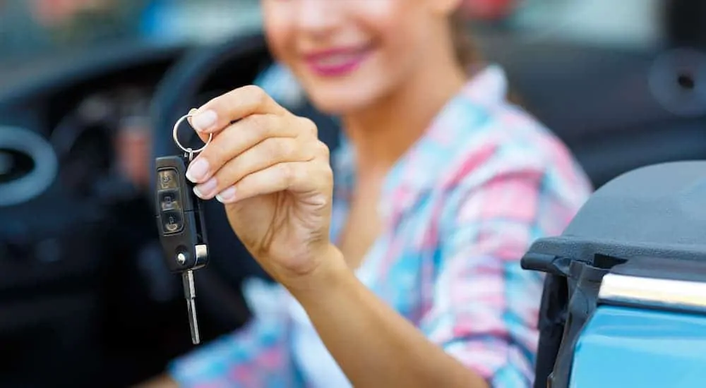 A woman is holding a car key while sitting inside a blue car.