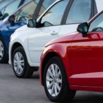 A row of different colored used cars for sale is shown.