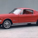 A red 1965 Ford Mustang fastback is against a grey background.