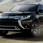 A 2019 Mitsubishi Outlander is driving around a corner in front of hills.