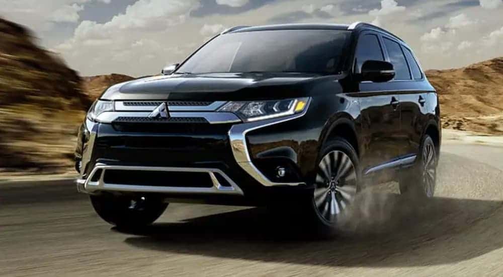 A 2019 Mitsubishi Outlander is driving around a corner in front of hills.