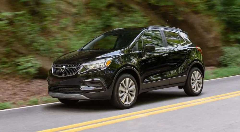 A black 2020 Buick Encore is driving past trees after winning the 2020 Buick Encore vs 2020 Chevy Trax comparison.