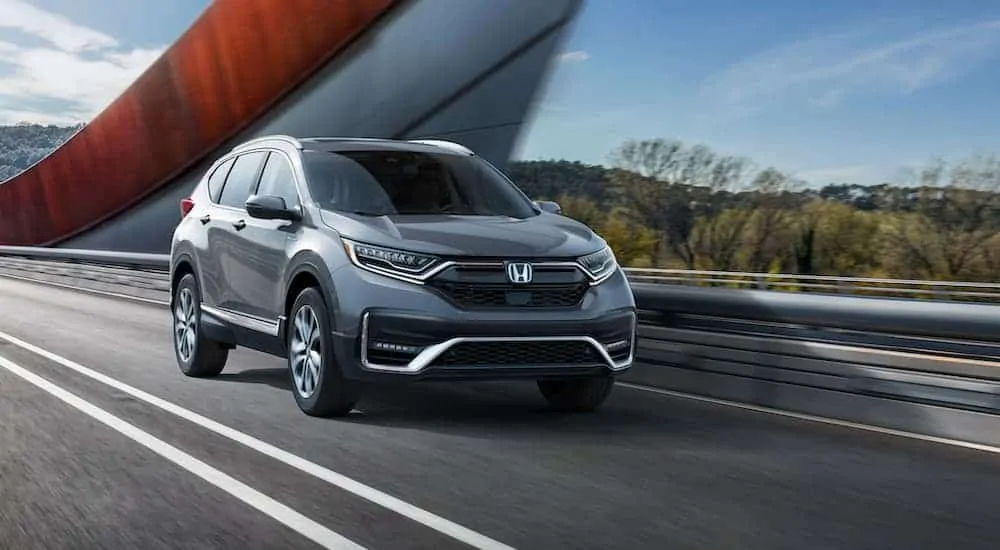 A grey 2020 Honda CR-V Hybrid is driving across a bridge with red design accents.