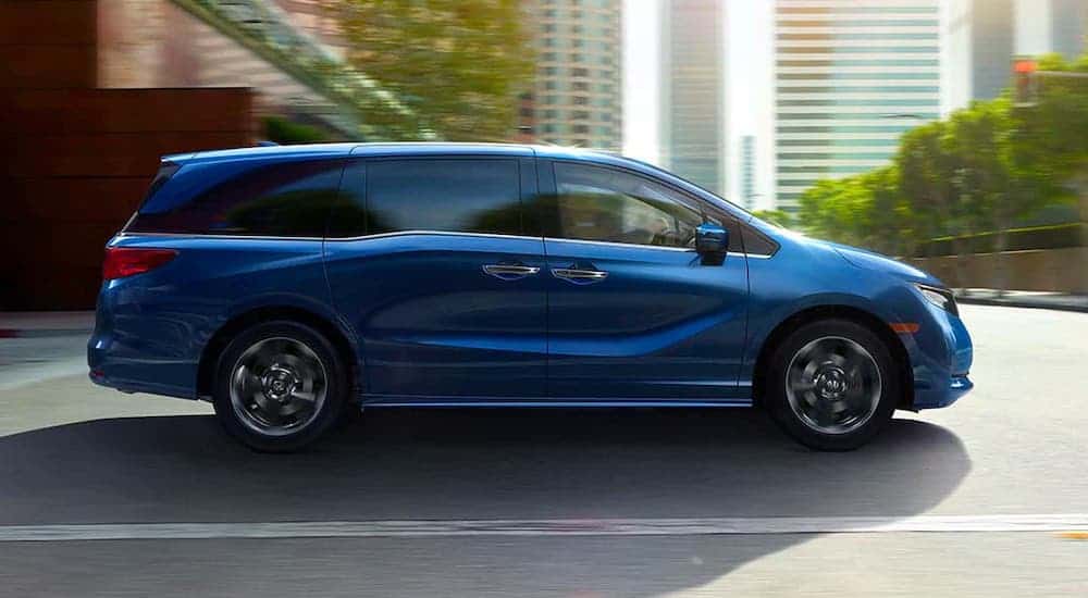 A blue 2020 Honda Odyssey is shown from the side driving in a city.