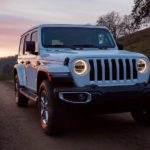 A white 2020 Jeep Wrangler Unlimited is shown from the front on a dirt road at dusk.