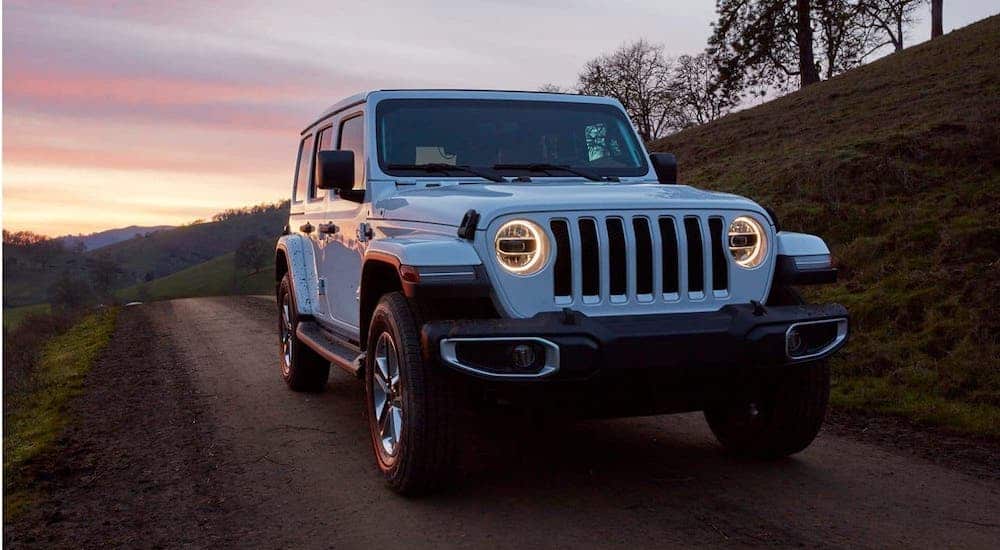 A white 2020 Jeep Wrangler Unlimited is shown from the front on a dirt road at dusk.