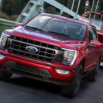 A red 2021 Ford F-150 is towing a boat across a bridge.