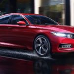 A popular new Honda for sale, a red 2020 Honda Accord, is driving on a city street in the rain.