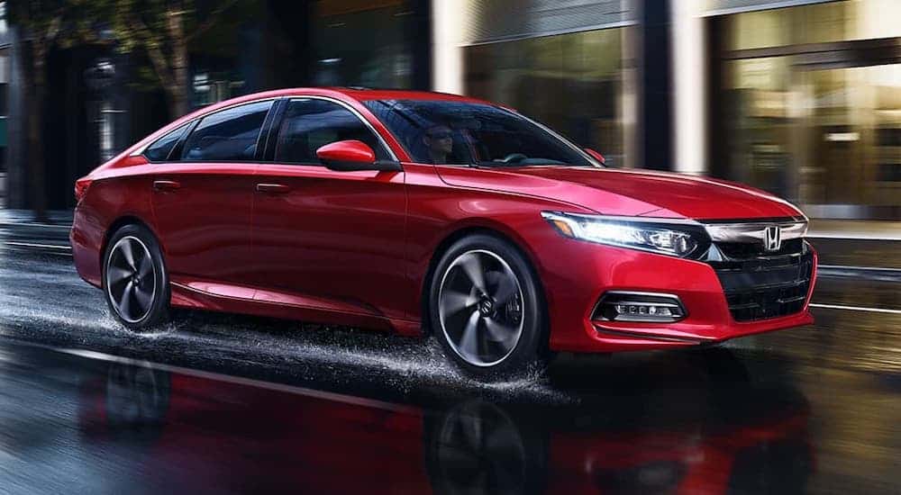 A popular new Honda for sale, a red 2020 Honda Accord, is driving on a city street in the rain.