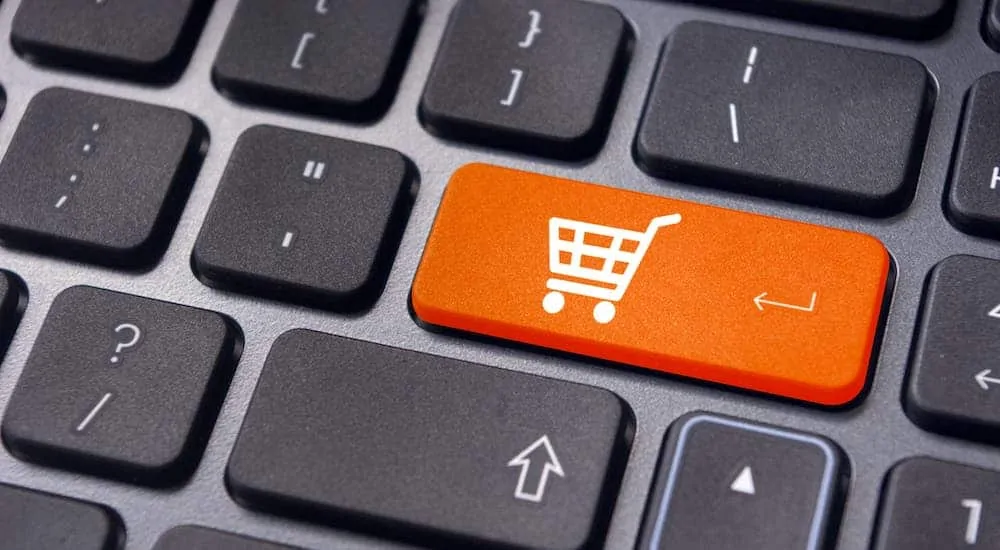 A closeup of a black keyboard is shown and one of the keys is replaced with an orange shopping cart button.