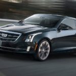 A black used Cadillac for sale, a 2019 Cadillac ATS, is driving on a blurry city street.